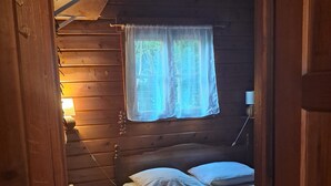 A wooden cabin room with a bed, a window with curtains, a lamp, and a door.