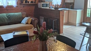 A wooden cabin interior with a dining table, a sofa, a kitchen area, and a ceiling light fixture.