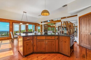 A spacious kitchen with wooden cabinets, a large island, and a view of the outdoors. - Hill Country Retreat Near Villa Antonia - Two Homes, Pool, Lake Views & Private Trails (Jonestown)