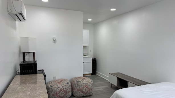 A modern hotel room with a bed, a small kitchenette, a seating area, and a built-in air conditioning unit. - Modern Suite Near Hot Springs & Ouachita River (Malvern)