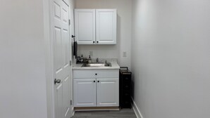 A narrow hallway leading to a kitchen with white cabinets, a sink, and a small black appliance. - Modern Suite Near Hot Springs & Ouachita River (Malvern)