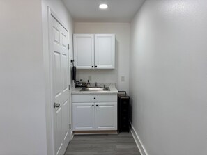 A narrow hallway leading to a kitchen with white cabinets, a sink, and a small black appliance.