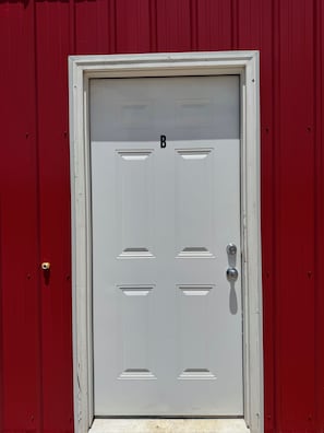 A white door with a numeric keypad, set in a red building.