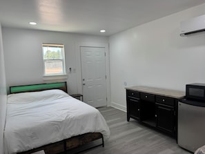 A bedroom with a bed, a desk, a refrigerator, and a door.