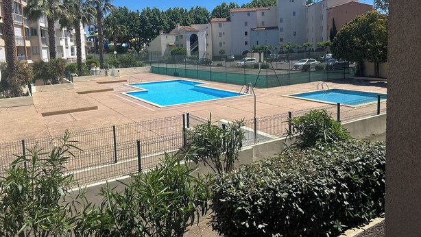 A residential area with two swimming pools, a fenced tennis court, and multi-story buildings in the background. - Nauticap cap d'agde (Agde)