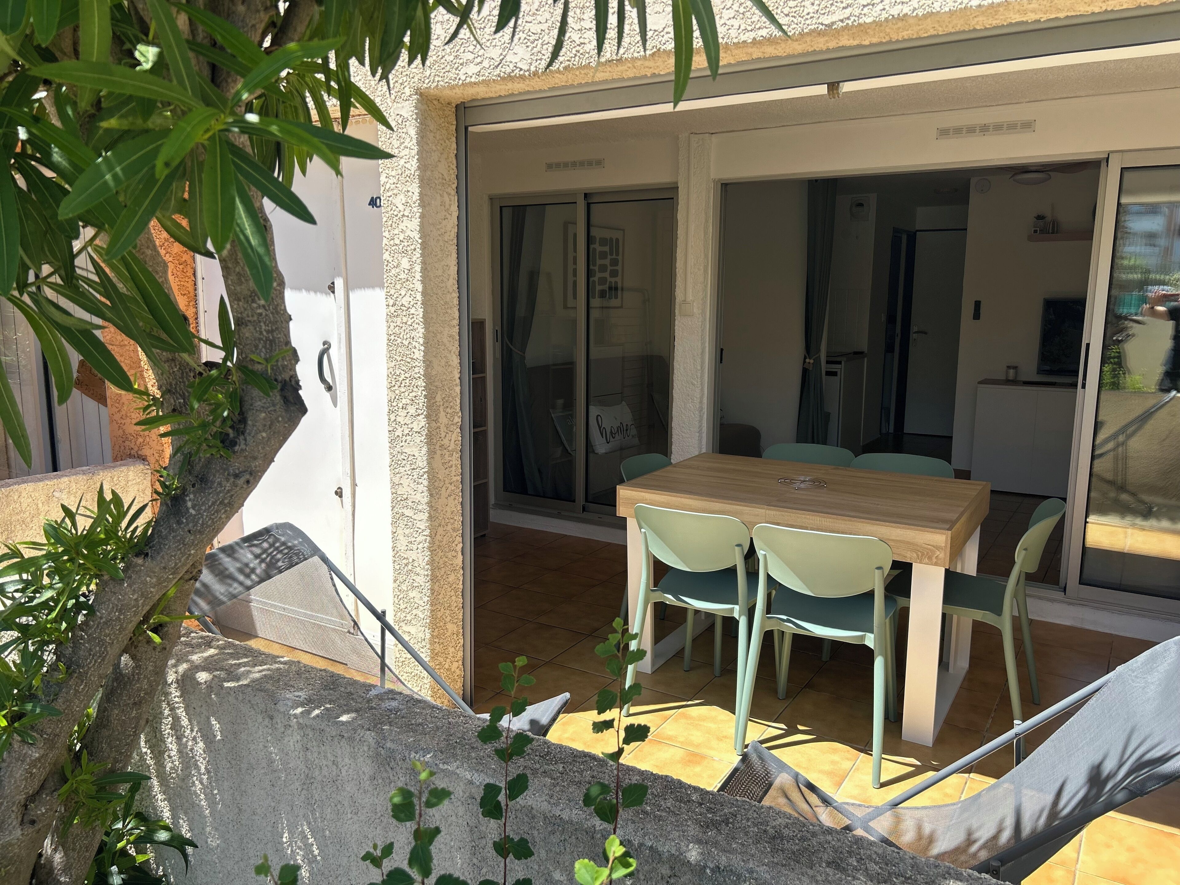 A patio with a wooden table and chairs, a sliding glass door leading to an interior space, and a stone wall with greenery.