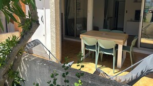 A patio with a wooden table and chairs, a sliding glass door leading to an interior space, and a stone wall with greenery. - Nauticap cap d'agde (Agde)
