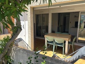 A patio with a wooden table and chairs, a sliding glass door leading to an interior space, and a stone wall with greenery. - Nauticap cap d'agde (Agde)