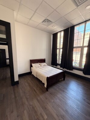 Ein Schlafzimmer mit einem Holzbett, einem Fenster mit Vorhängen und Blick auf Gebäude.