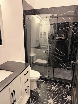 Ein Badezimmer mit einer gläsernen Duschkabine, einer weißen Toilette und einem schwarzen Marmorboden.