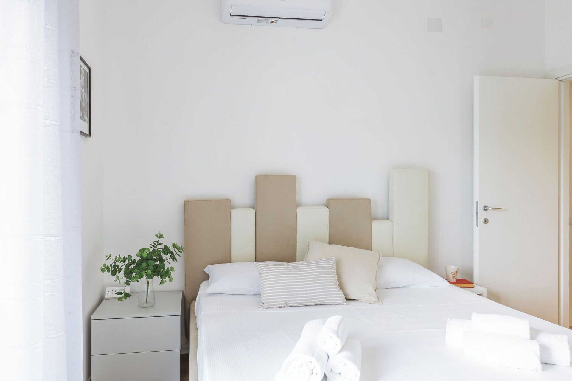 A hotel room with a bed, bedside table, and an air conditioning unit.