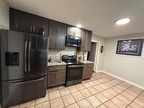 A kitchen with dark cabinets, stainless steel appliances, a microwave, and a tiled floor. - Charming 3-bedroom house in wonderful St. Louis with AC (St. Louis)