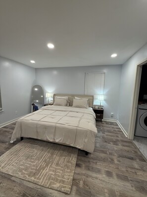 A bedroom with a large bed, a bedside table with a lamp, a wall-mounted mirror, and a washing machine in the corner. - Charming 3-bedroom house in wonderful St. Louis with AC (St. Louis)