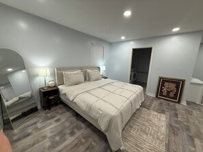 A bedroom with a bed, bedside tables, a mirror, a framed picture, and a door leading to a laundry area. - Charming 3-bedroom house in wonderful St. Louis with AC (St. Louis)