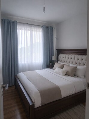 Une chambre à coucher avec un grand lit, une table de chevet avec une lampe et une fenêtre avec des rideaux.