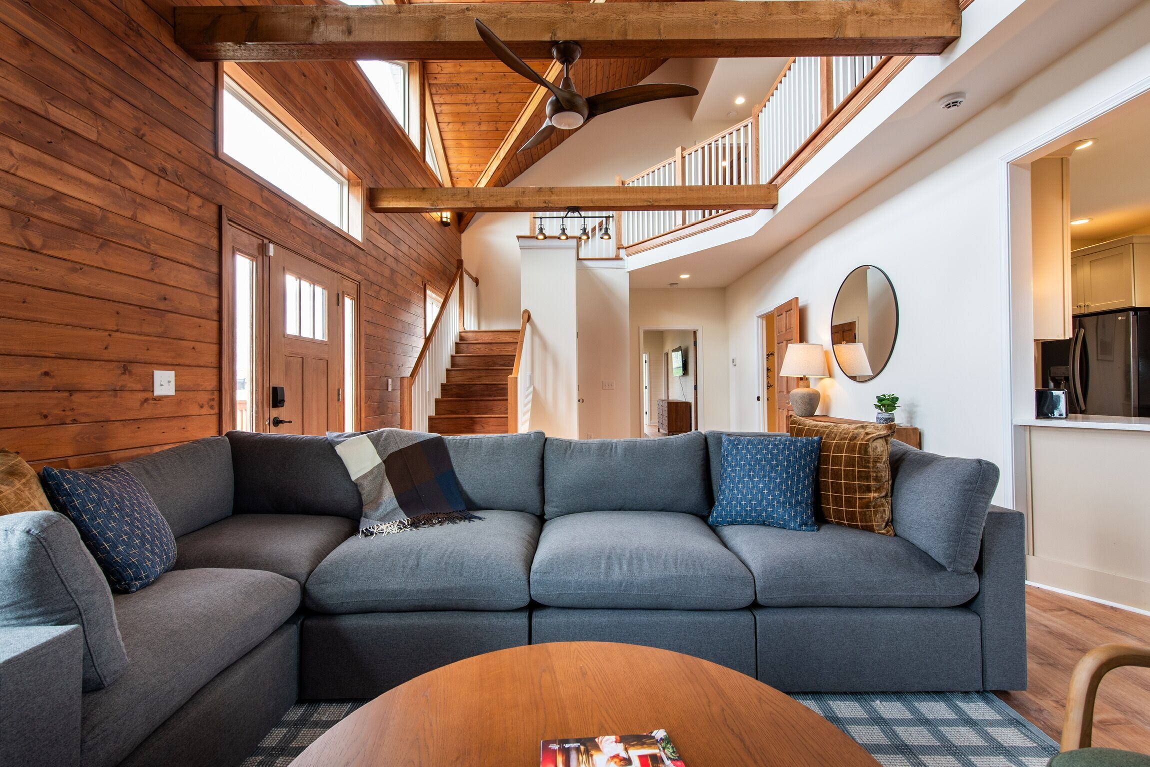 Ein modernes Wohnzimmer mit einem Ecksofa, einer Holzbalkendecke und einer Treppe, die zu einer oberen Ebene führt.