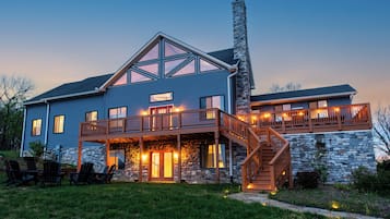 A two-story house with a stone chimney, a wooden deck, and a staircase leading to the upper level.