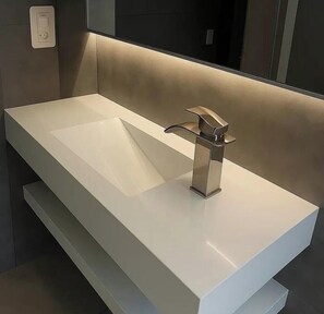 Ein modernes Badezimmer mit einem großen weißen Waschbecken, einem Chromarmaturen und einem Spiegel darüber.