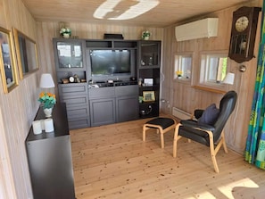 Un espacio habitable compacto con kitchenette, televisor de pantalla plana, piso de madera, sillón de cuero negro y una ventana con cortinas.