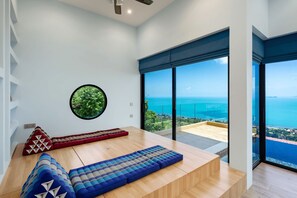 A modern room with a large window, a circular wall decoration, and a wooden bench. - Panoramic Escape - 3BR Empress Villa (adult only) (Koh Samui)