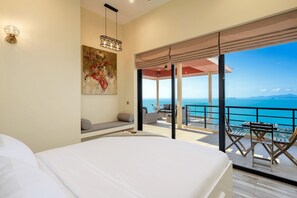 Ein Schlafzimmer mit einem großen Bett, einem Gemälde, einer Deckenleuchte und einem Balkon mit Meerblick.