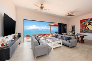 A modern living room with a large window, a flat-screen TV, and a dining area with a view of the ocean. - Panoramic Escape - 3BR Empress Villa (adult only) (Koh Samui)