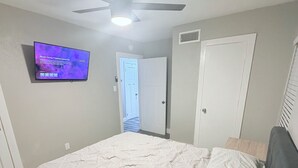 A bedroom with a bed, a ceiling fan, a TV, and a door. - Charming 3-bedroom house in brilliant Fort Worth with AC (Fort Worth)