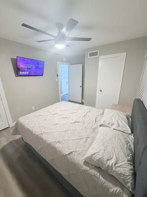 A bedroom with a bed, a ceiling fan, a TV, and a door. - Charming 3-bedroom house in brilliant Fort Worth with AC (Fort Worth)