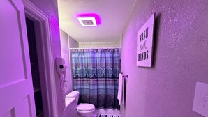 A narrow bathroom with a toilet, a shower curtain, a towel rack, and a sign that says 'WASH YOUR HANDS'. - Charming 3-bedroom house in brilliant Fort Worth with AC (Fort Worth)