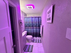 A narrow bathroom with a toilet, a shower curtain, a towel rack, and a sign that says 'WASH YOUR HANDS'. - Charming 3-bedroom house in brilliant Fort Worth with AC (Fort Worth)