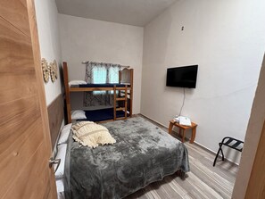 A bedroom with a bunk bed, a flat-screen TV, a small bedside table, and a chair.