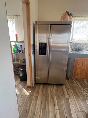 Un refrigerador de acero inoxidable con dispensador de agua, un armario de madera y un protector de salpicadura de azulejos en una cocina.