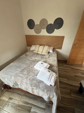 Una cama bien hecha con cabecera de madera, dos almohadas y dos toallas dobladas con un diseño de trébol.
