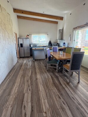 A modern kitchen with a built-in refrigerator, a dining area with a wooden table and chairs, and a stone wall.