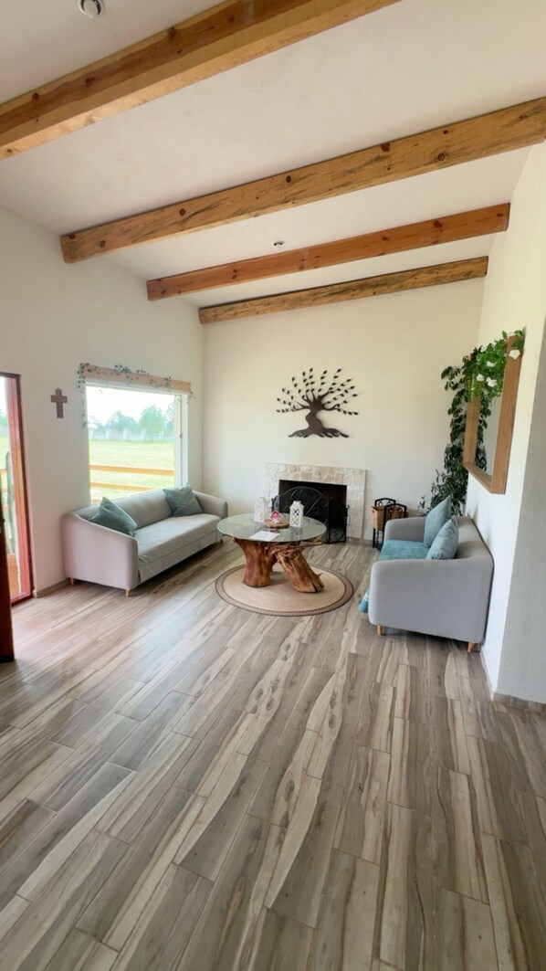 A spacious living room with a fireplace, two sofas, a coffee table, and wooden beams on the ceiling.