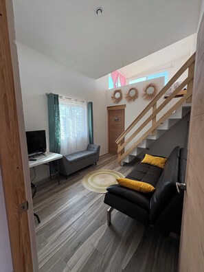A living room with a sofa, a desk, a TV, a staircase, and a door.