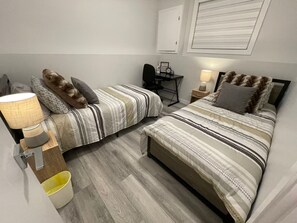 Ett sovrum med två sängar, ett skrivbord, en stol, en lampa och en papperskorg.