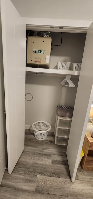 Ett kompakt förvaringsutrymme med trägolv, en vit korg och plastförvaringslådor.