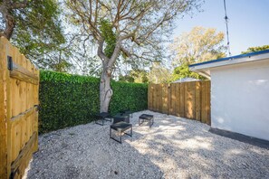 A backyard with a tree, a wooden fence, and a white building. - Adorable 2-bedroom house next to Hard Rock Casino (Fort Lauderdale)