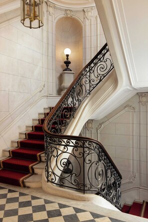 A grand staircase with ornate black railings, red carpeted steps, and a chandelier. - Luxury Flat -2br/6p- Madeleine/saint Honore (Paris)