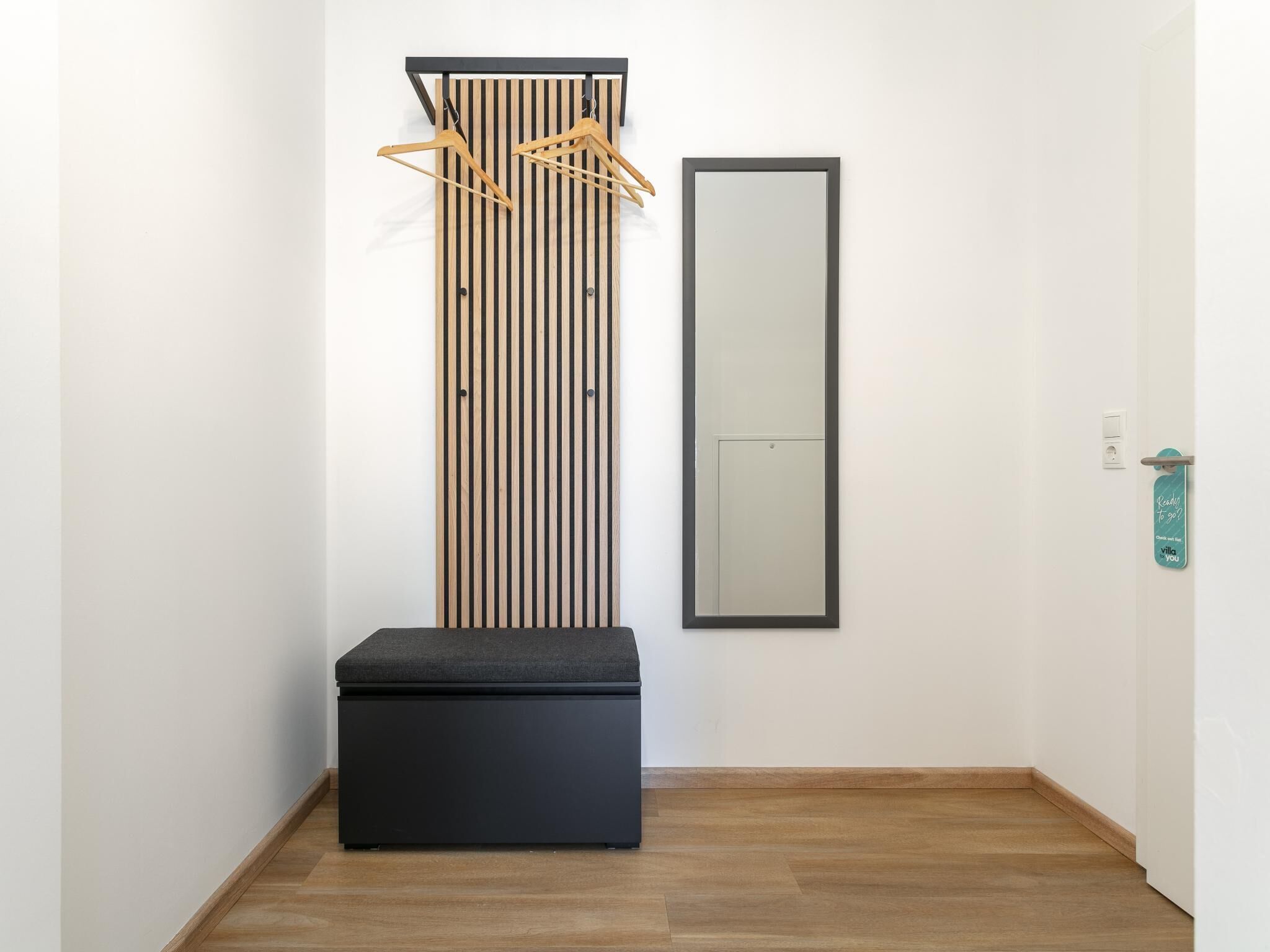 Ein Korridor mit einer schwarzen Bank, einer vertikalen Holzwandverkleidung und einem Spiegel an der Wand.