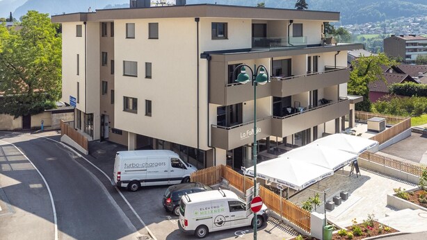 Ein mehrgeschossiges Gebäude mit einem Restaurant im Erdgeschoss, einem Parkplatz mit einem weißen Lieferwagen und einer Bergbäckergrund in der Ferne.