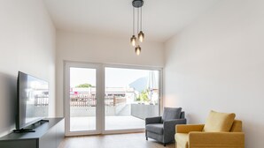 Ein modernes Wohnzimmer mit Flachbildfernseher, einer Couch und einem Sessel, mit einer Schiebeglastür zu einem Außenbereich.