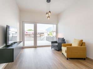 A modern living room with a flat-screen TV, a sofa, and a chair, with a sliding glass door leading to an outdoor area. - Modern holiday apartment with terrace in Jenbach (Jenbach)