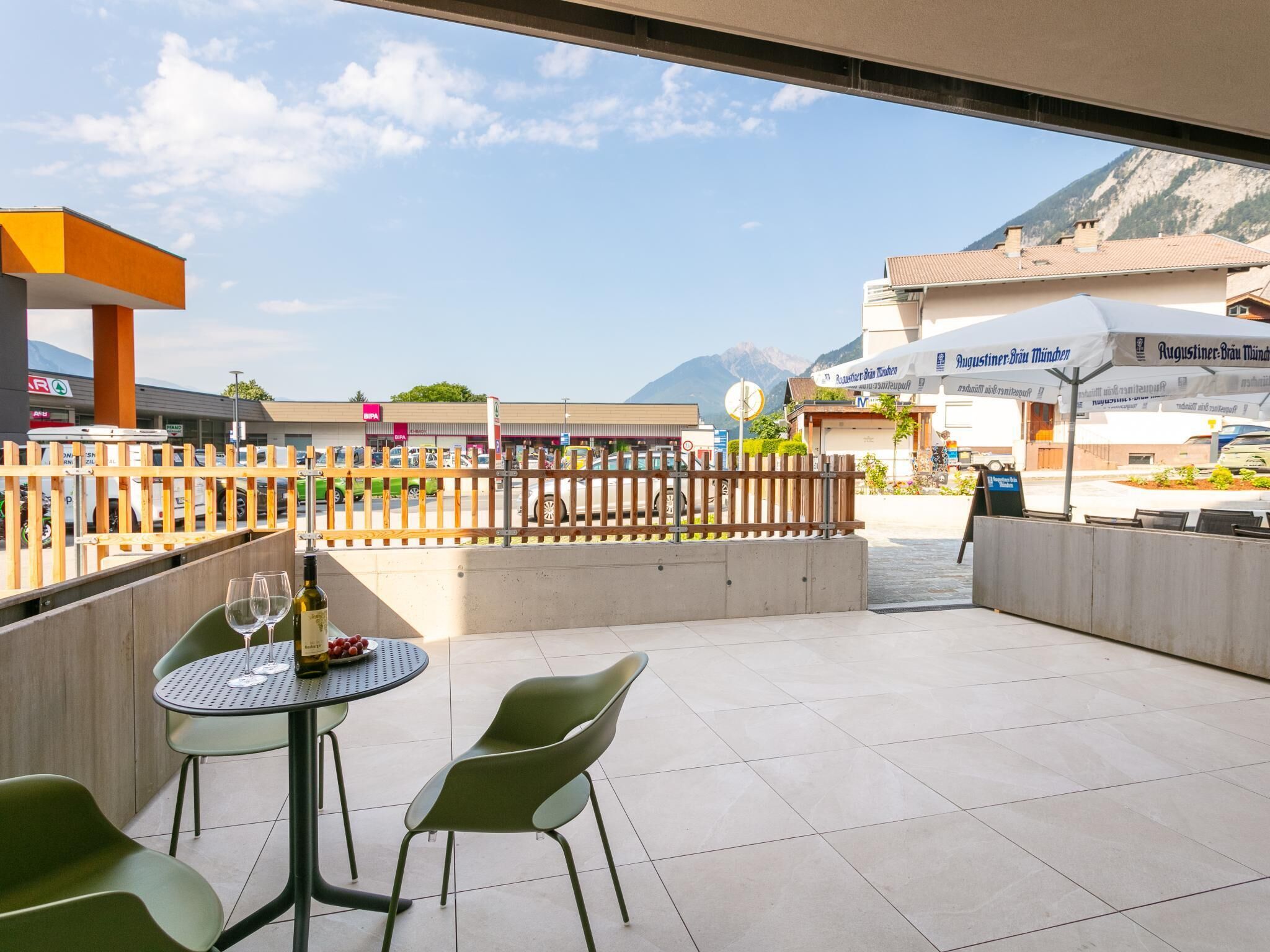 An outdoor patio area with a table and chairs, a bottle of wine, and a view of a mountain in the background.
