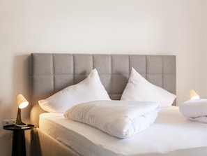 A neatly made bed with white bedding and pillows, a grey upholstered headboard, and two bedside lamps on a nightstand. - Modern holiday apartment with terrace in Jenbach (Jenbach)