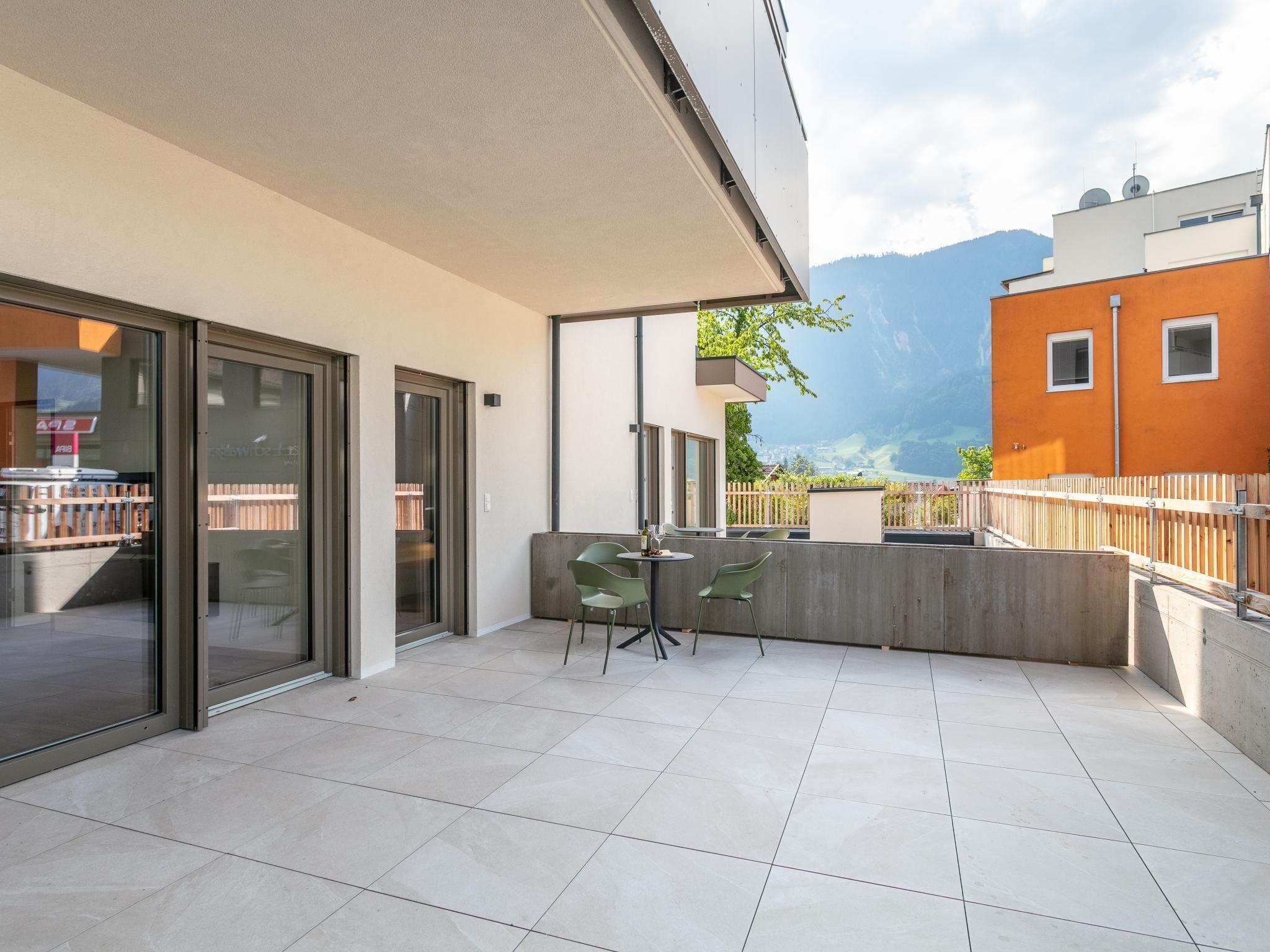 A modern outdoor terrace with a dining area, large sliding glass doors, and a view of a mountain.