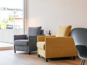 Two armchairs with different fabric colors, a wine bottle, and a glass on a table, with a view of a street sign outside. - Modern holiday apartment with terrace in Jenbach (Jenbach)
