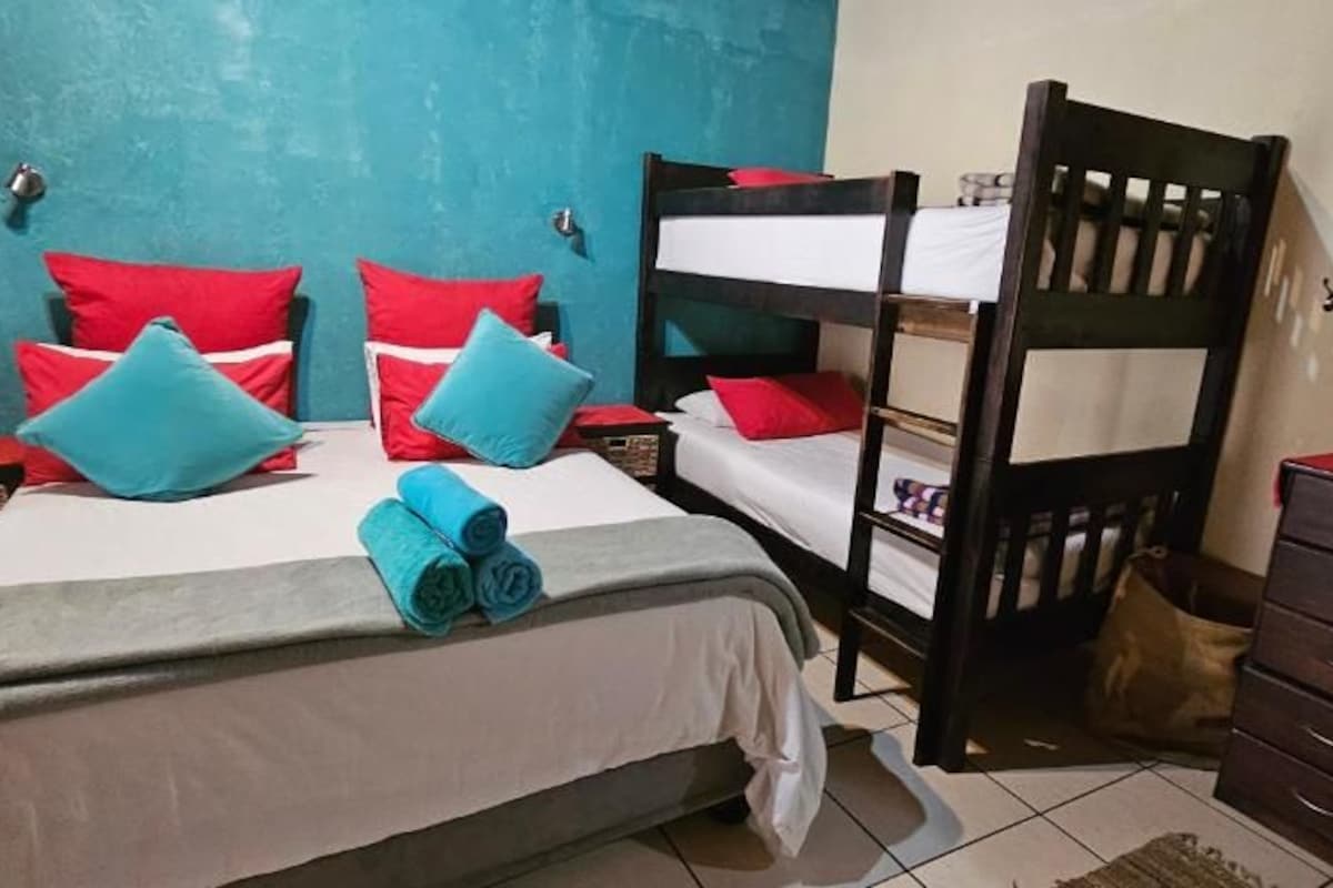 A room with bunk beds, a bed with rolled towels, a dresser, and a framed picture on the wall.