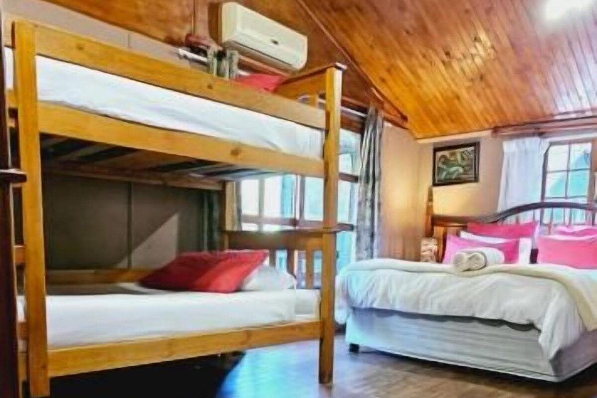 A room with wooden flooring, bunk beds, a single bed, and a window with curtains.